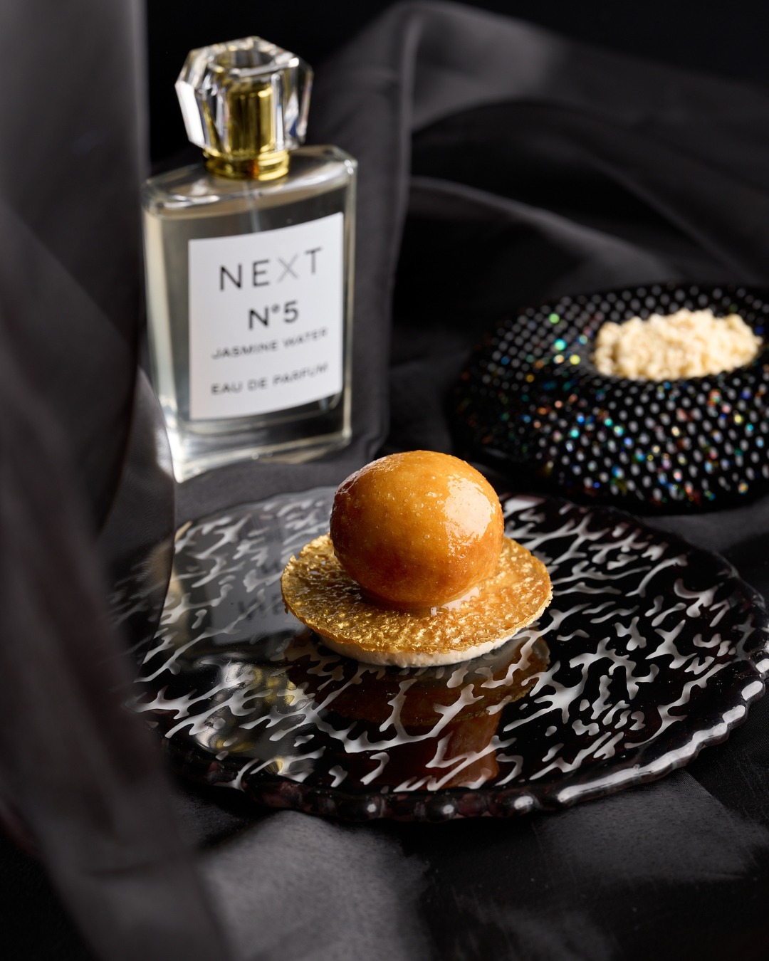 Glazed brioche doughnut beside a perfume bottle and a dish of frozen jasmine pearls at Next Chicago