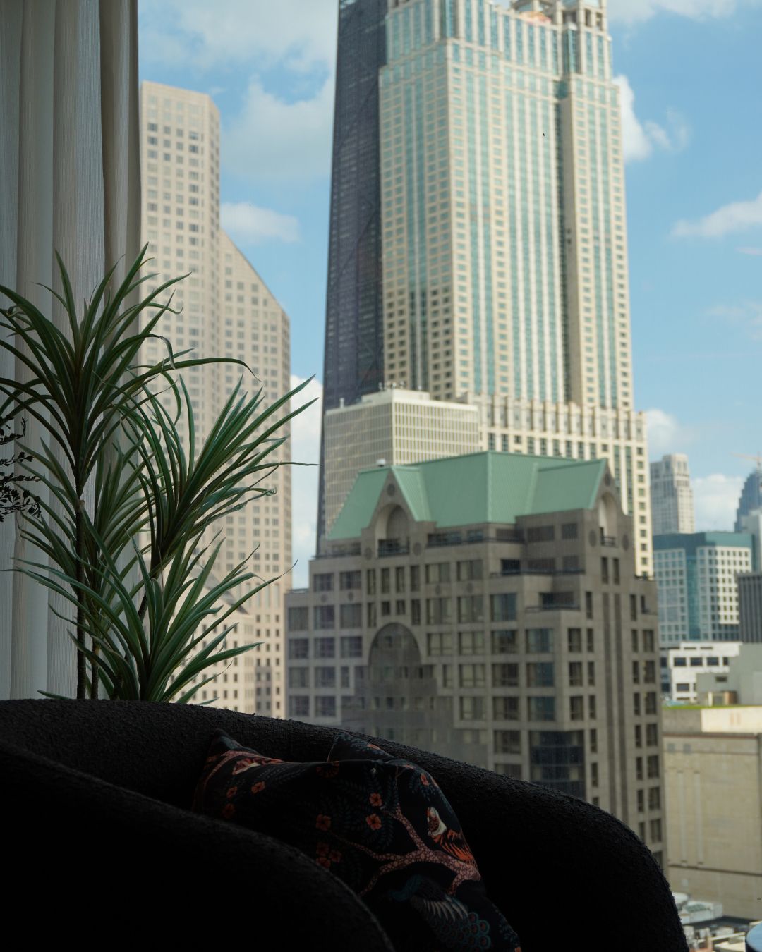 A lounge chair and greenery framing a Gold Coast skyline view through the windows at Pandan