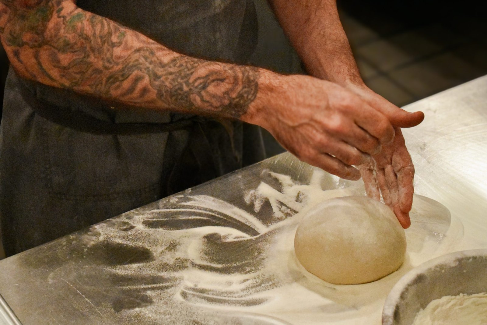 Chef Andrew Ashmore in an apron stretching a sheet of pizza dough by hand in the kitchen