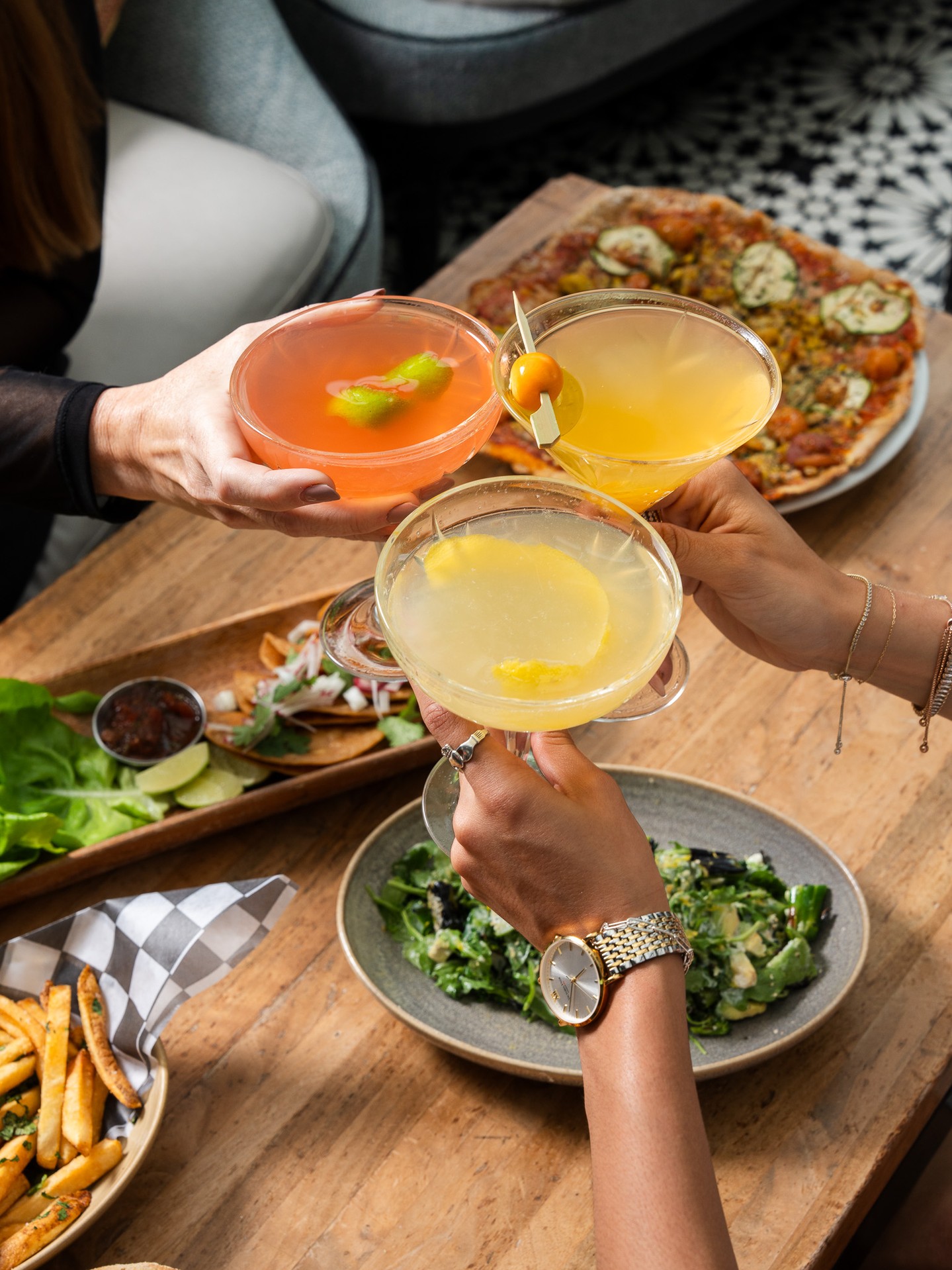 Cocktails raised over pizza, salad and fries at a table at ROOF on theWit