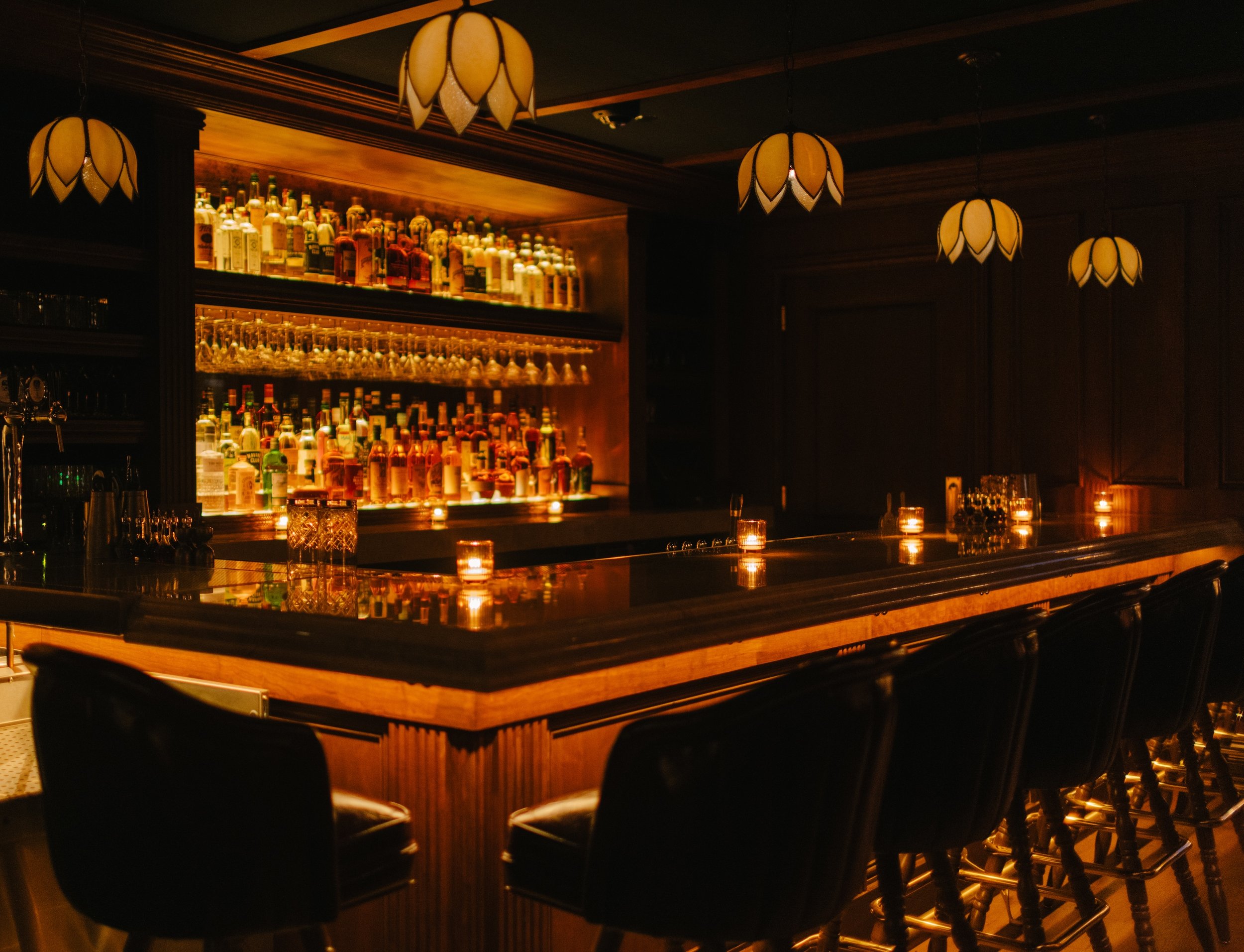 Candles glow along the small wood bar with backlit bottle shelves and tulip pendant lights at The Bull Moose