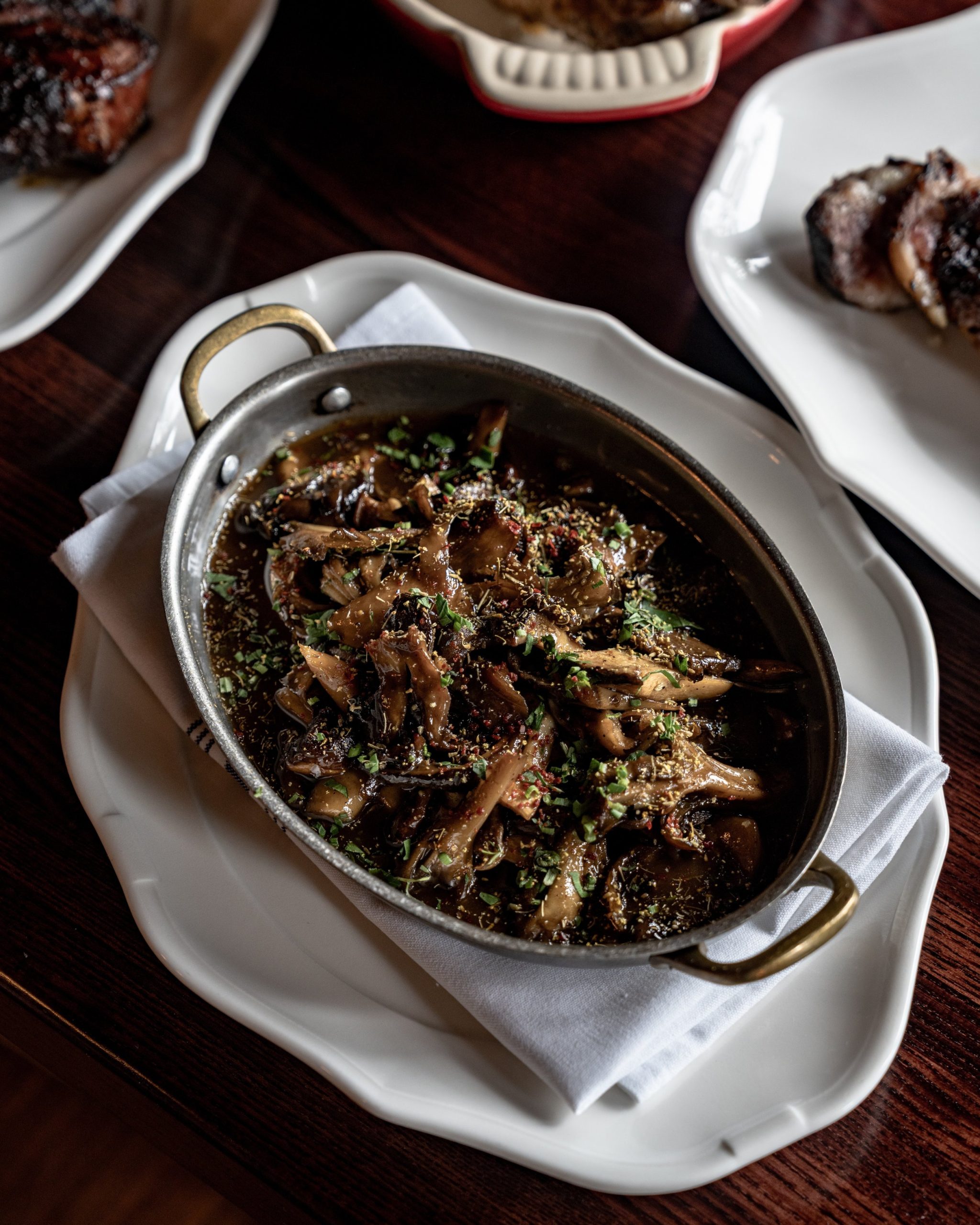 Mushrooms au jus in a small silver oval dish set beside a sliced steak at The Bull Moose