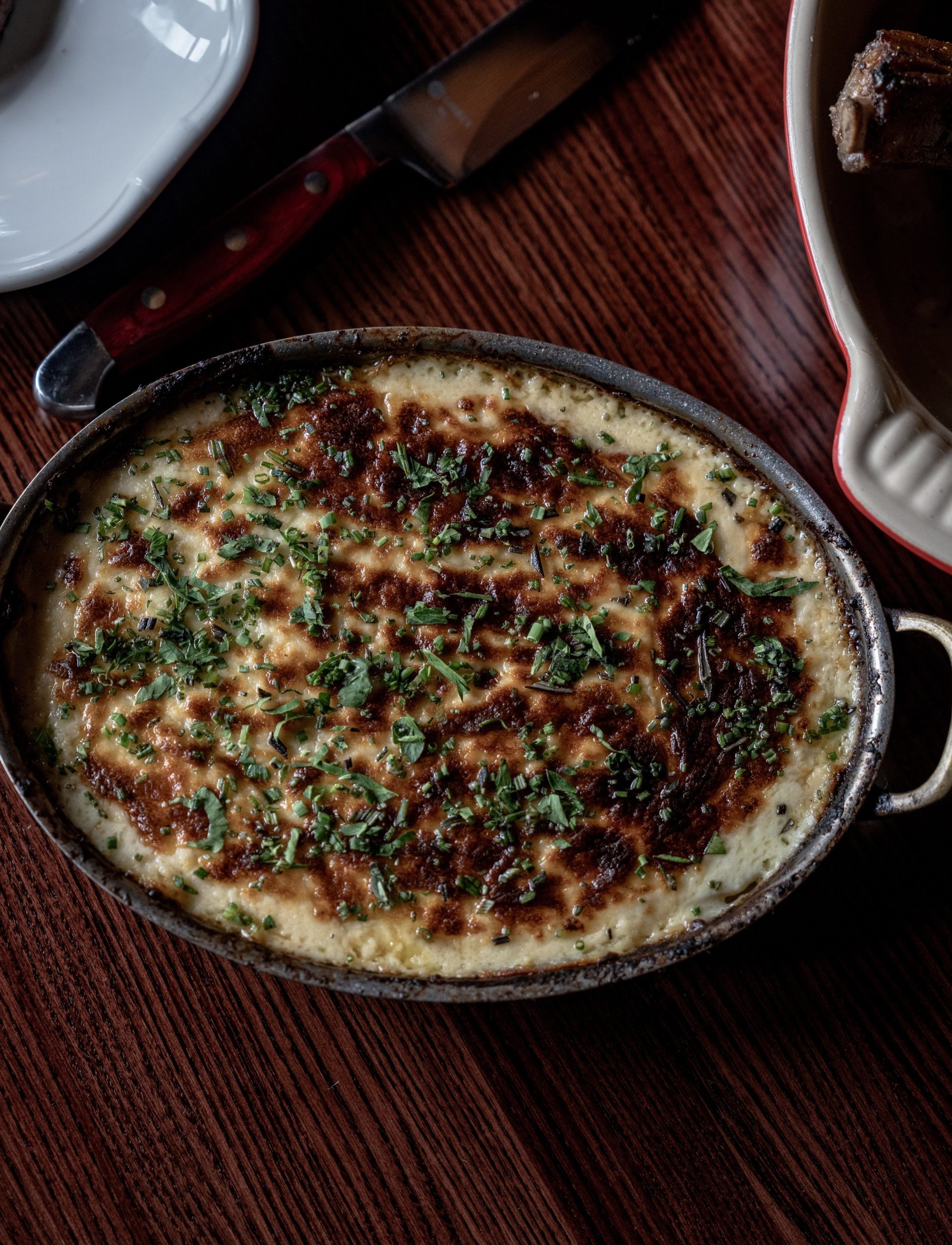 A bubbling skillet of potatoes au gratin with a browned cheese crust and fresh herbs at The Bull Moose