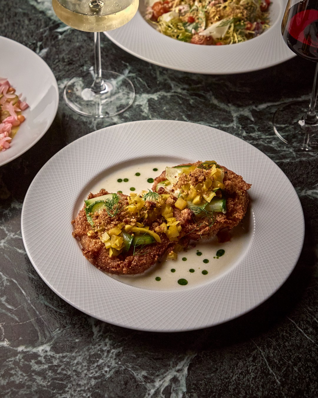 Fried heirloom tomato slices topped with chow chow and herbs on a white plate at The Ives