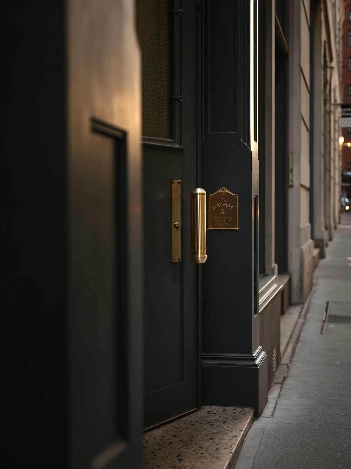 Black door with a polished brass handle and The Wayman brass plaque at the Fulton Market entrance
