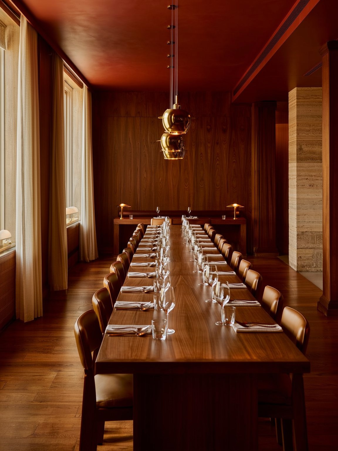 A long walnut dining table set with wine glasses under gold pendant lights at The Wayman Chicago