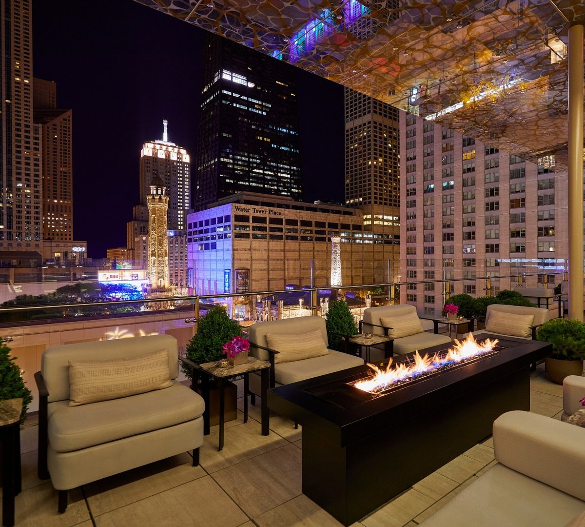 A lit fire table and lounge seating on the terrace at Z Bar, The Peninsula Chicago, at night